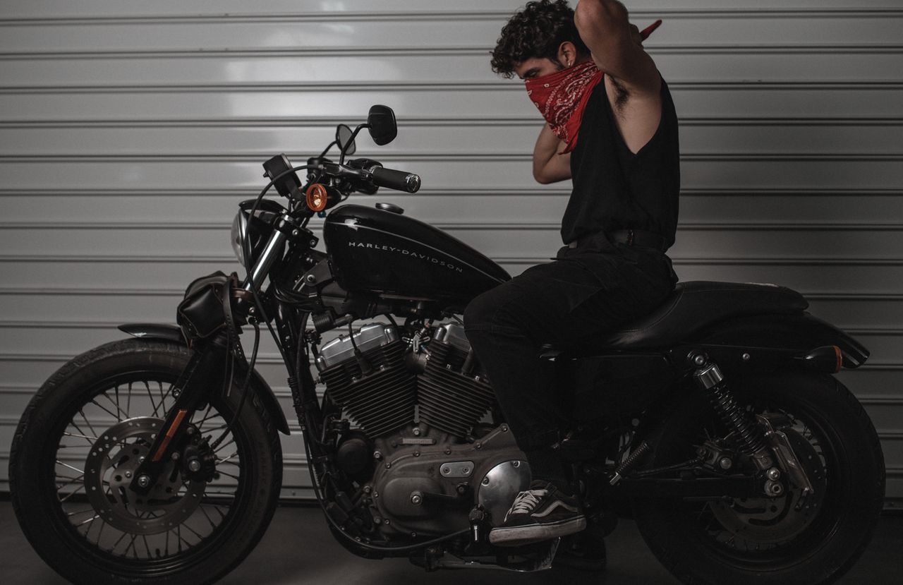 A man with a bandana sits on a Harley-Davidson motorcycle indoors.
