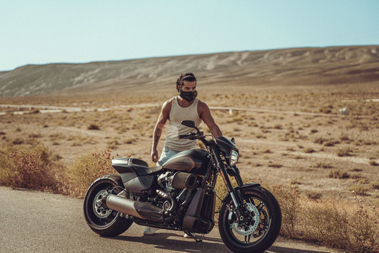 A man with a face mask stands by his motorcycle in the barren desert landscape of Baku.