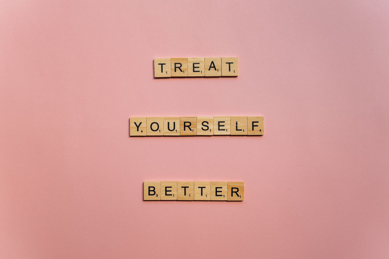 Wooden tiles on a pink background spelling 'Treat Yourself Better'. Ideal for self-care and motivation themes.